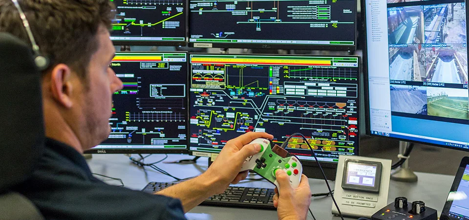 Operator at a remote operations control room with a wall of monitors showing site systems