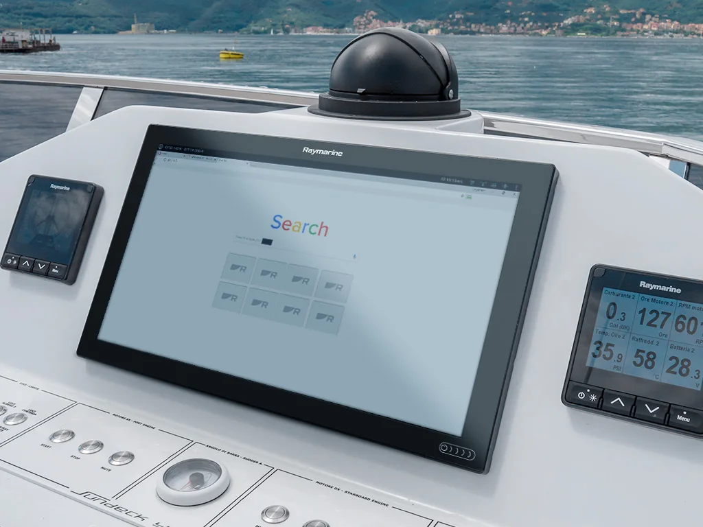 Vessel helm console with a large navigation display, instrument screens and a radar dome, looking out over the water
