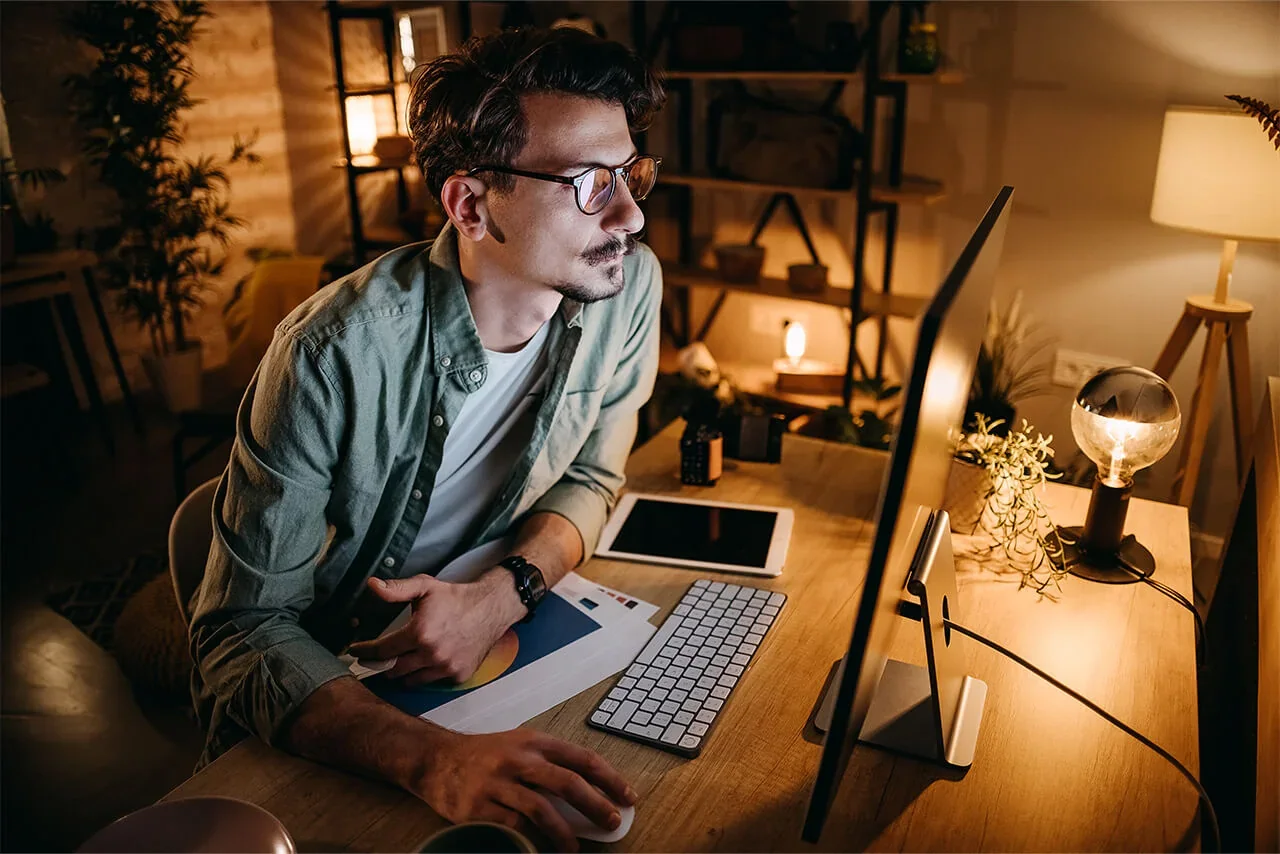 Person working late at a desktop PC with a large monitor in a home office