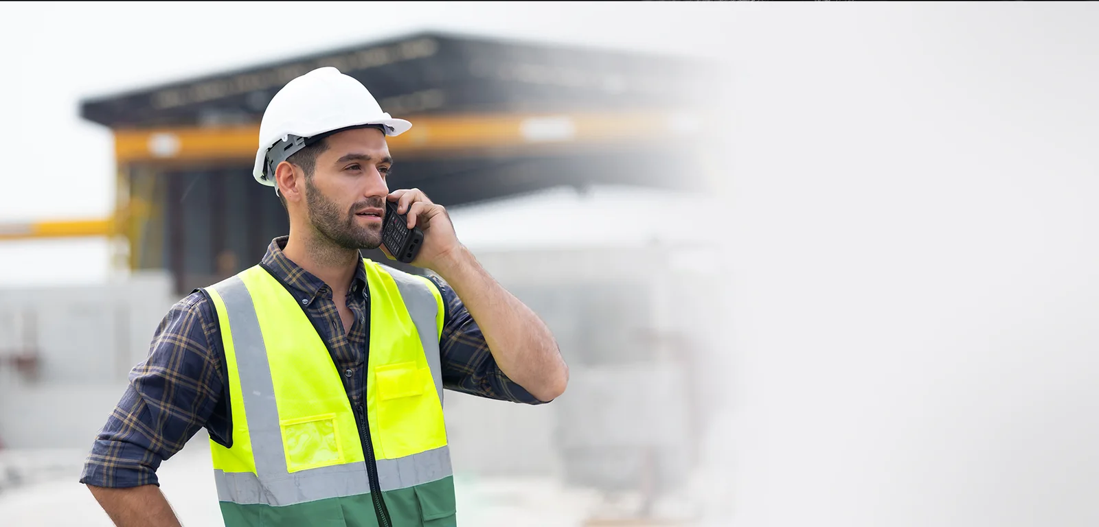 Site worker in a hard hat and hi-vis vest on a call with a Yealink AX86R rugged Wi-Fi phone