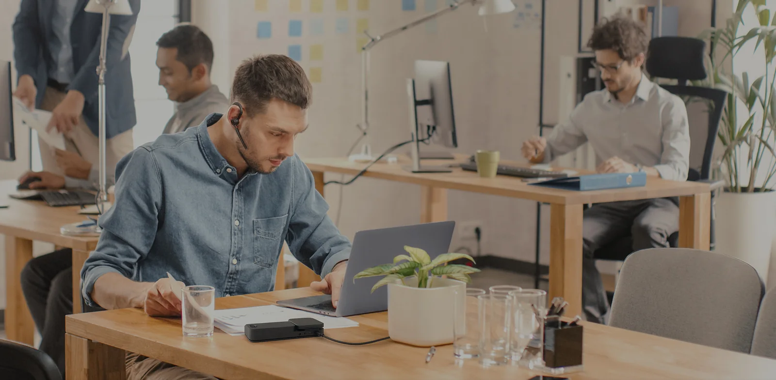 Office worker wearing a Yealink BH71 mono Bluetooth headset at a laptop in an open-plan office