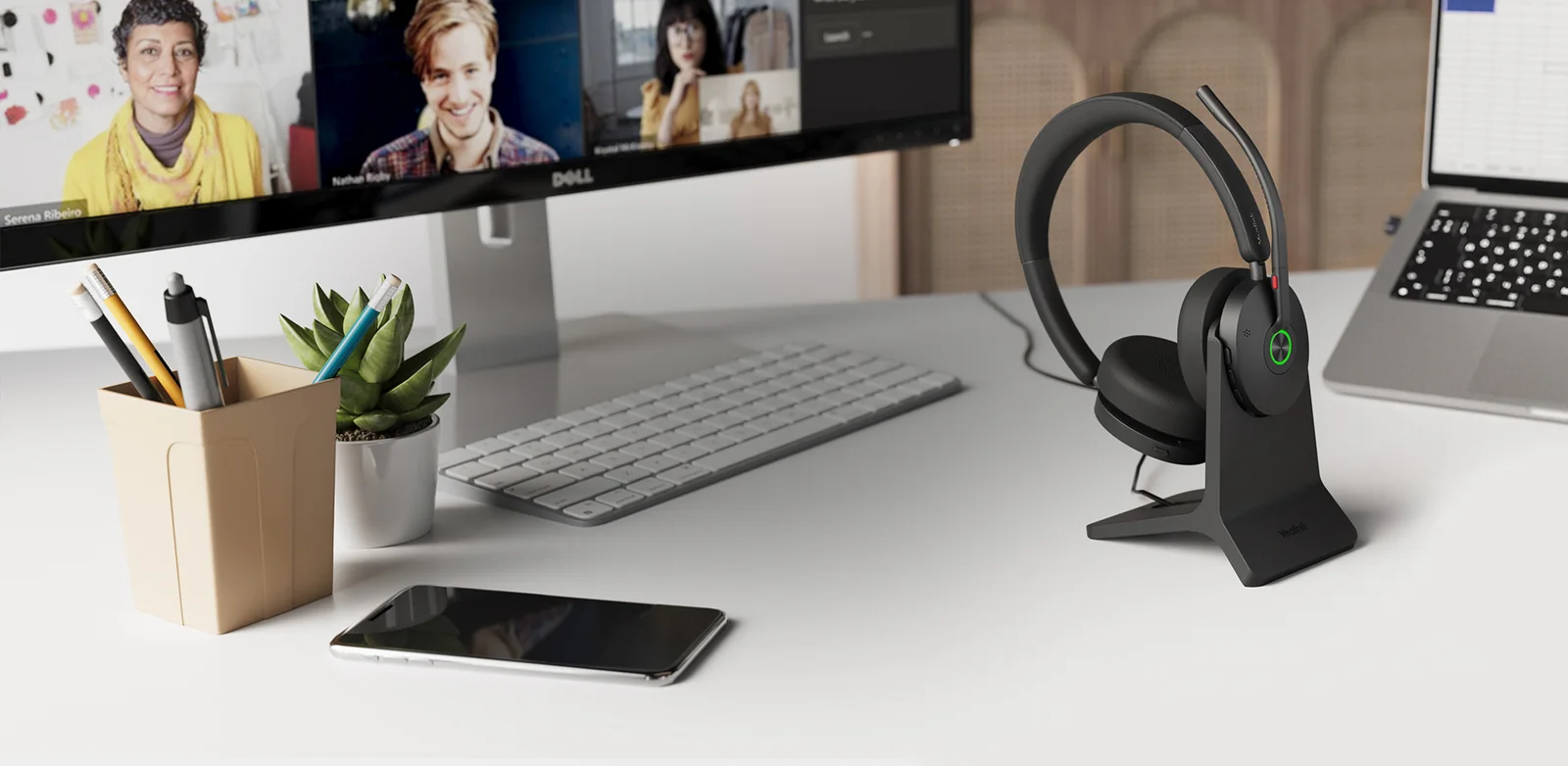 Yealink BH74 Bluetooth headset docked on its charging stand next to a monitor, keyboard and mobile on a home office desk
