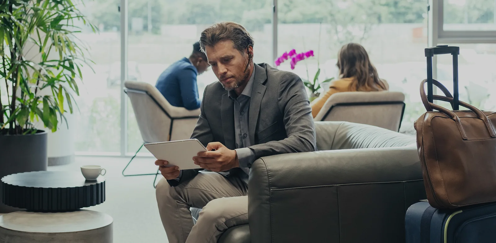 Businessman wearing a Yealink BH71 earpiece with a tablet in an airport lounge