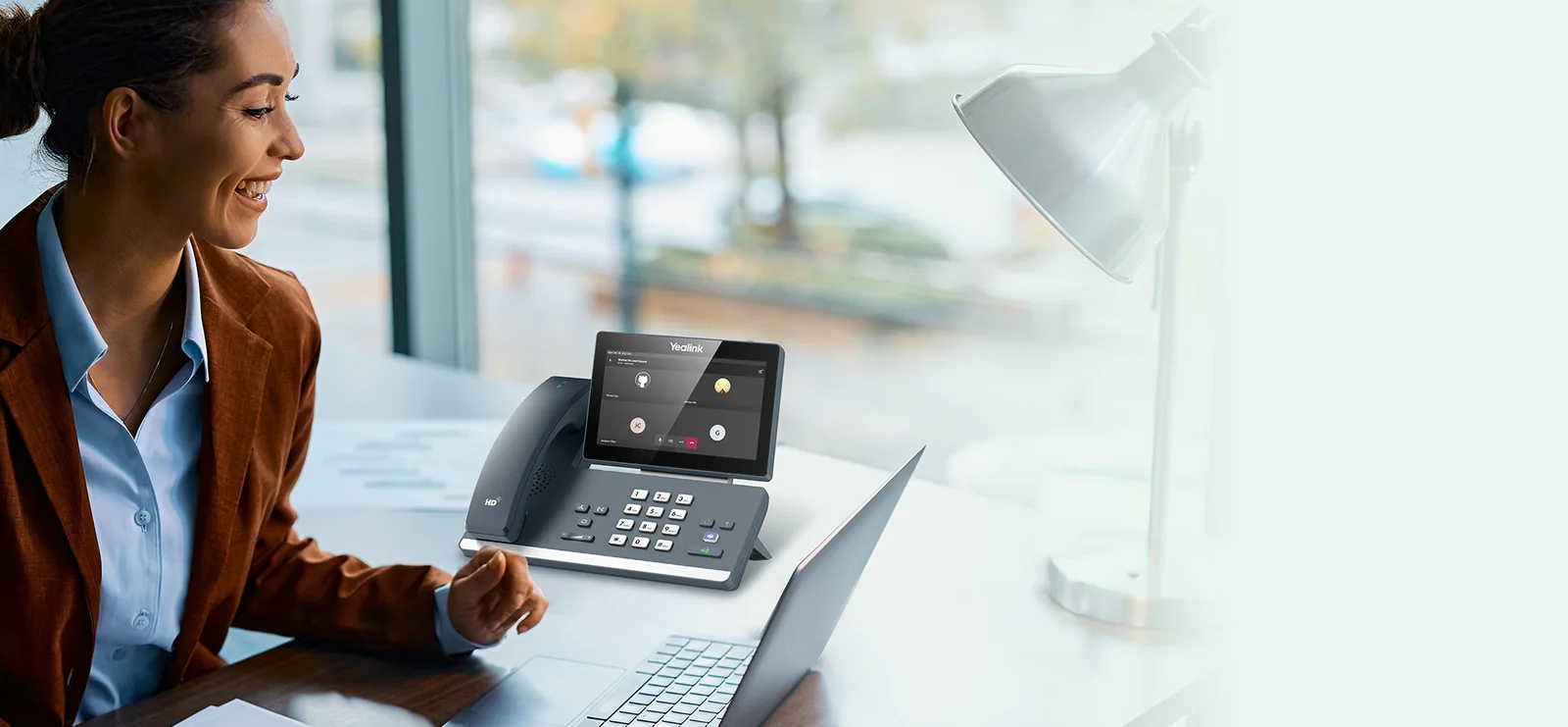 Professional at a desk with a Yealink MP58-WH E2 Microsoft Teams phone beside her laptop