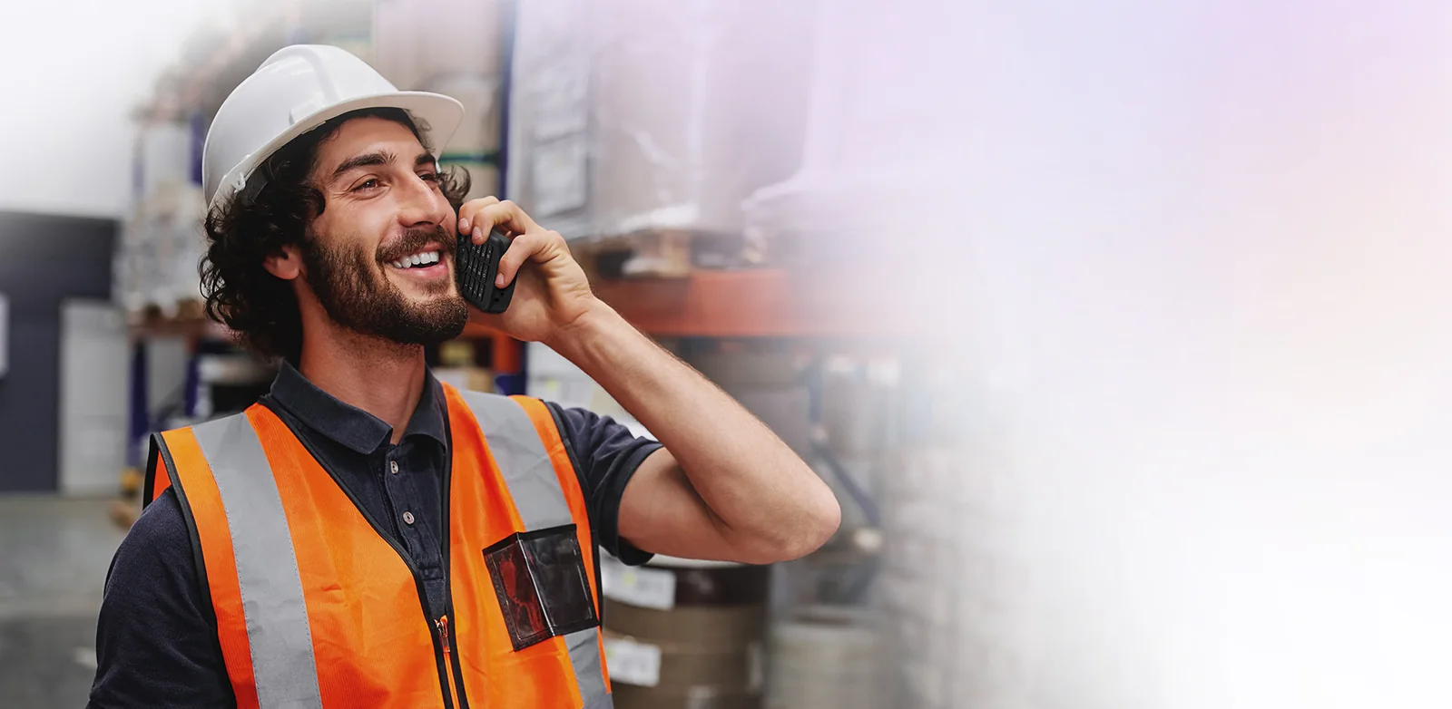 Warehouse worker in a hard hat and hi-vis vest talking on a Yealink MP66W Teams handset