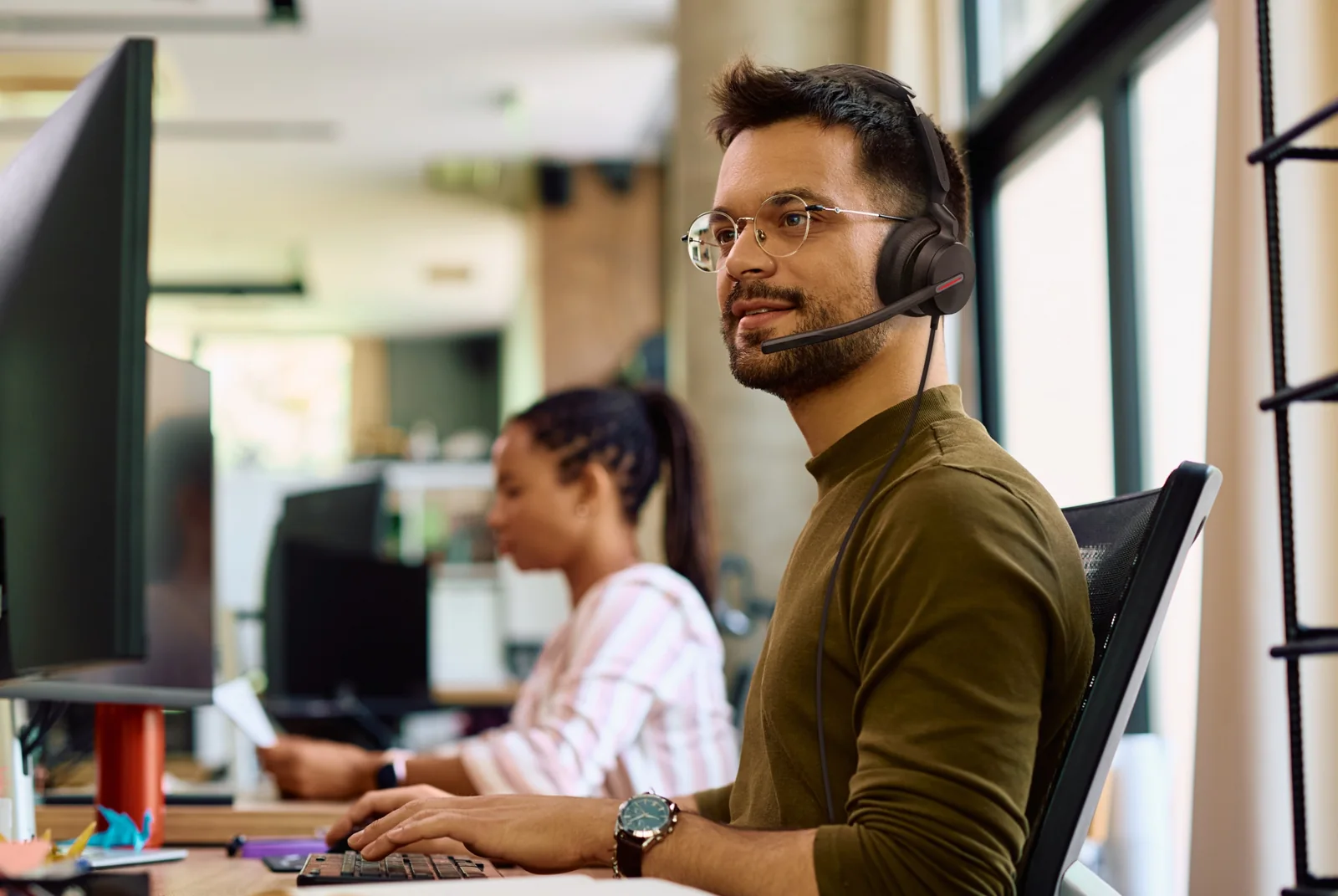 Man in an open-plan office on a call wearing a Yealink UH46 wired headset